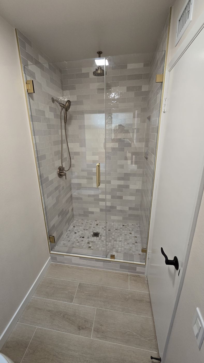 Walk-in shower with frameless glass, brushed gold hardware and pebble mosaic floor