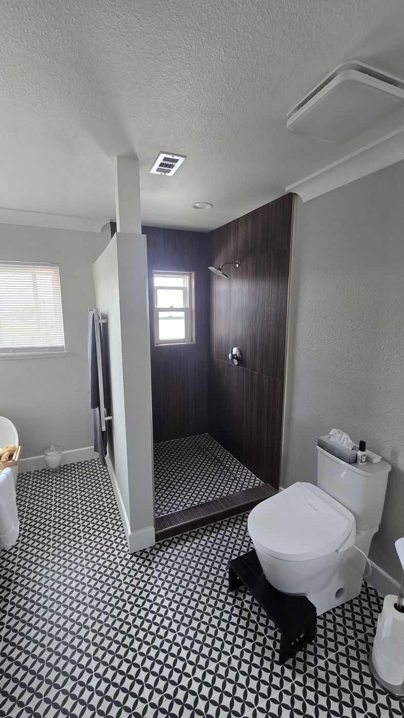 Primary bathroom walk-in shower with dark wood-look tile walls and black-and-white patterned floor tile