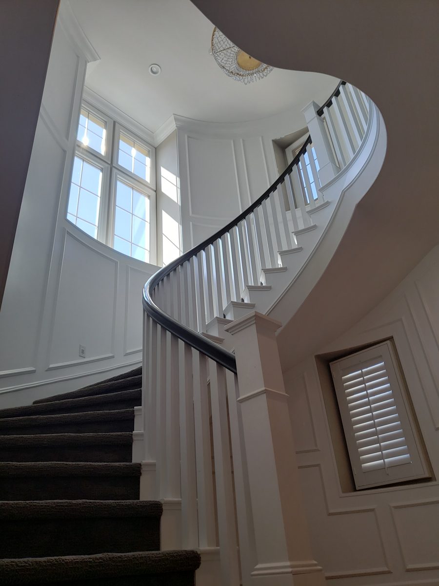 Curved staircase with dark stained handrail, white balusters and paneled walls